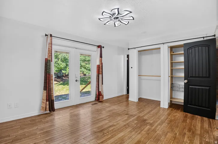 Hardwood-finish flooring throughout, featuring french doors with exterior access, a contemporary ceiling fixture, and a closet with built-in shelving