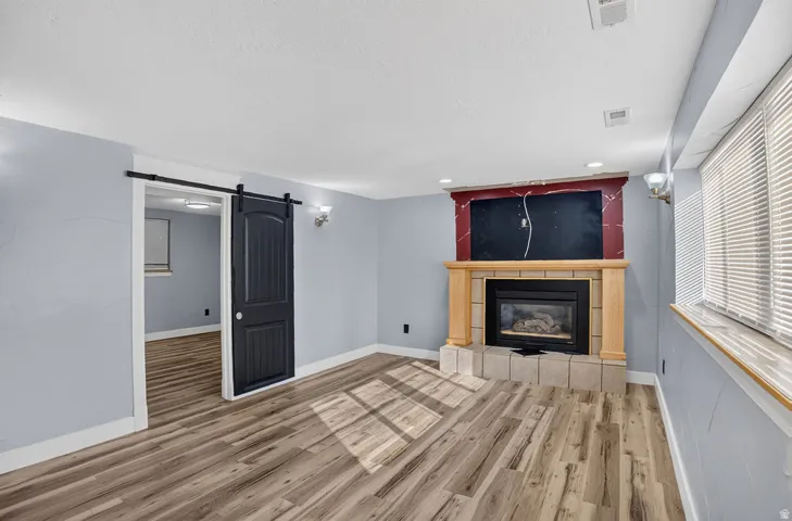 Living area featuring wood-finish flooring, a fireplace with a light-toned mantel, a dark barn door, and wall sconces