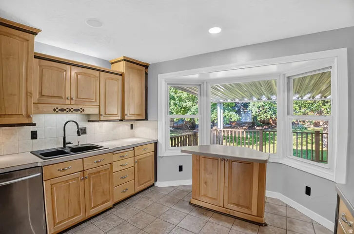 Kitchen featuring wood cabinetry, a stainless steel dishwasher, and a bay window overlooking a deck and backyard