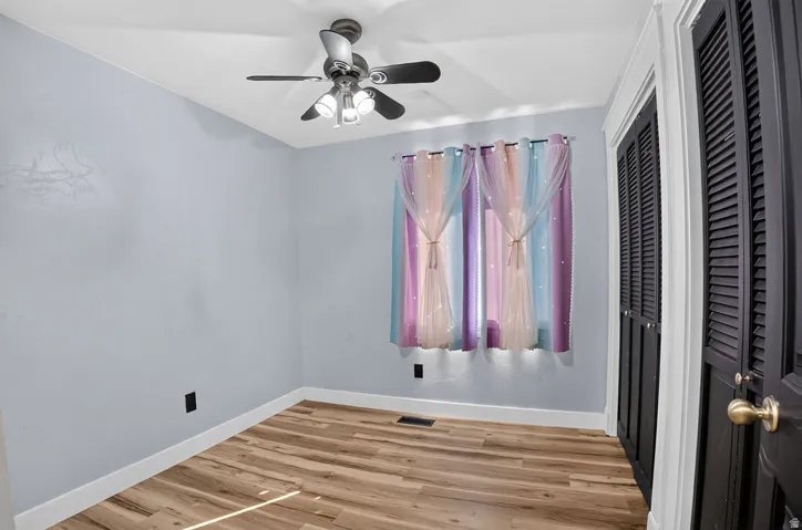 Room featuring wood-finish flooring, a ceiling fan with integrated lighting, and white baseboards