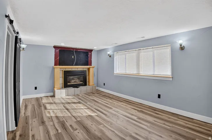 Interior space featuring wood-finish flooring, a fireplace with a light wood mantel and tile hearth, and a window with blinds