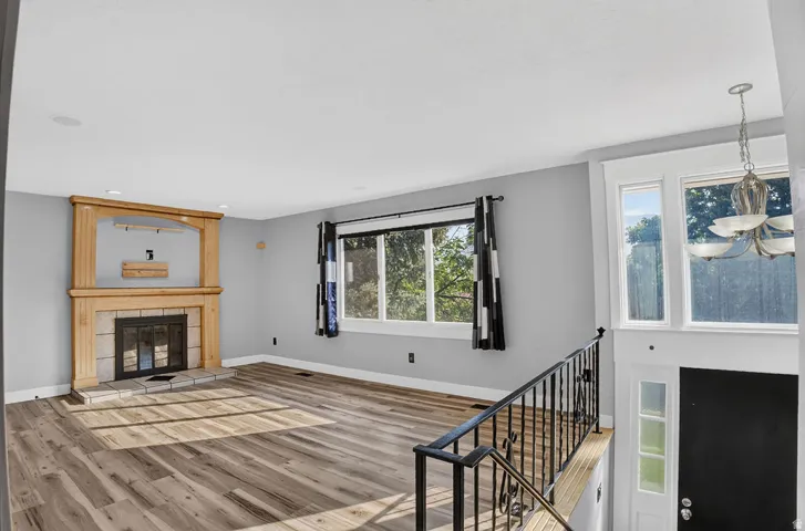 Spacious living area featuring wood-finish flooring, a wood mantel fireplace with stone surround, recessed lighting, and ample natural light from multiple windows