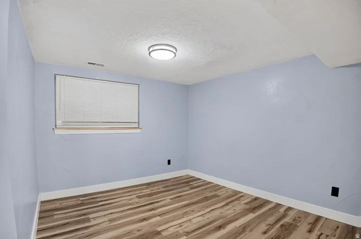 Room featuring wood-finish flooring, a window with blinds, and light blue walls with a textured finish