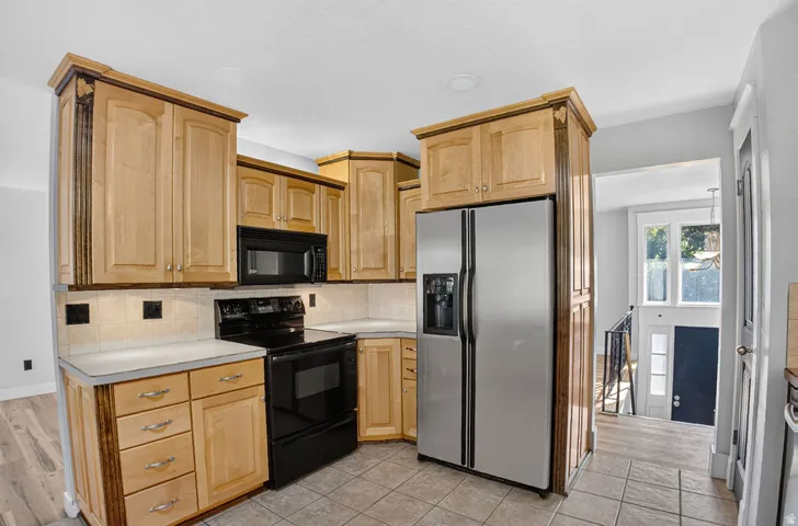 Kitchen featuring light wood cabinetry with darker accent trim, a stainless steel side-by-side refrigerator, and a black electric range with a built-in microwave