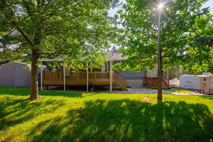 Rear exterior featuring a spacious wood deck with white posts, a separate exterior staircase, and mature trees providing natural shade