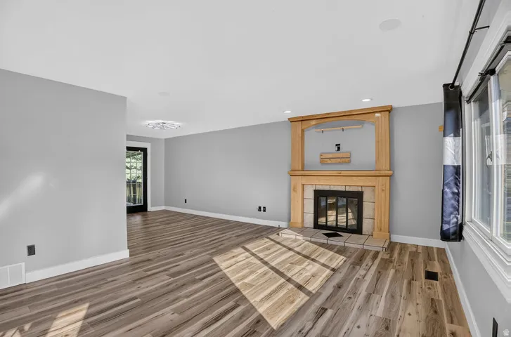 Spacious room featuring wood-finish flooring, a light gray color palette, and a prominent fireplace with a wood mantle and tile surround