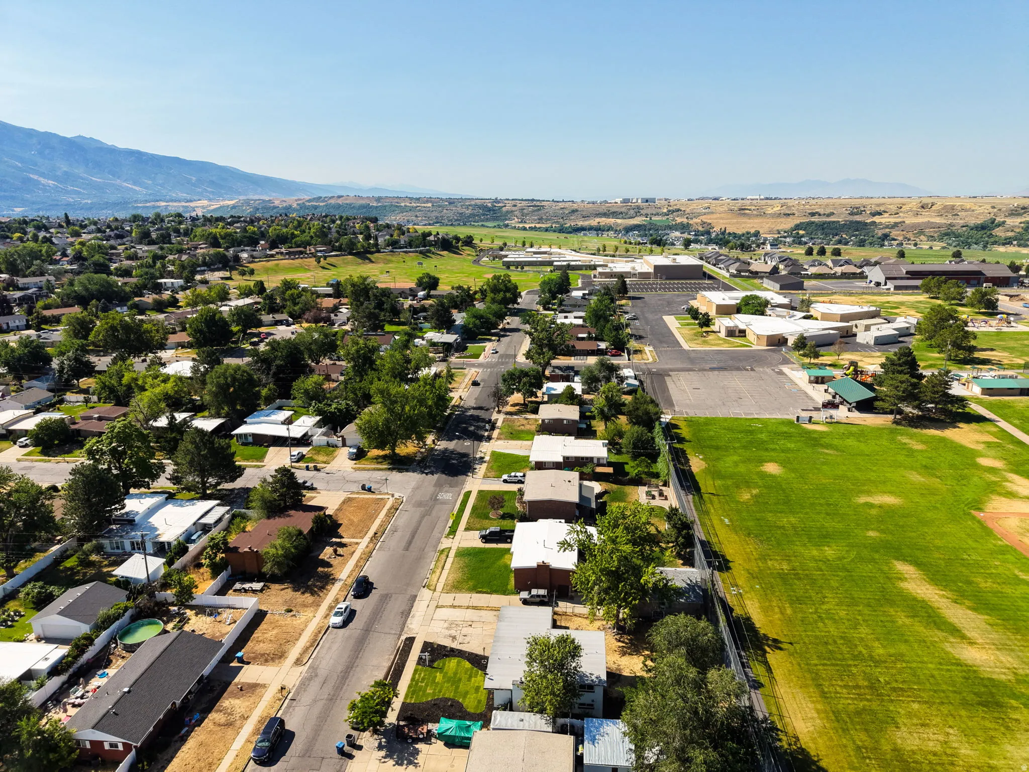 Aerial perspective showcasing a residential neighborhood with tree-lined streets, surrounded by green fields, and backed by distant mountains