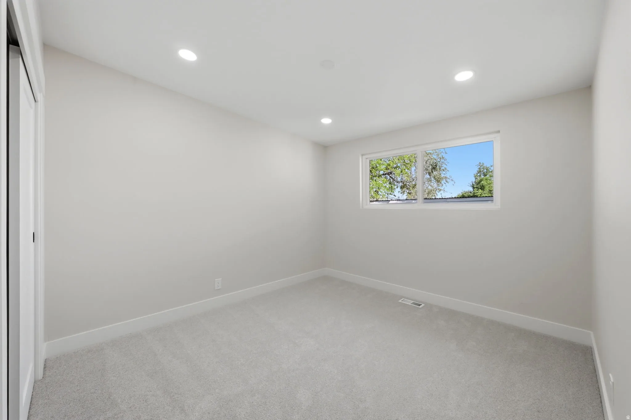 Neutral-toned room featuring a large window, recessed lighting, light gray carpeting, and white baseboards