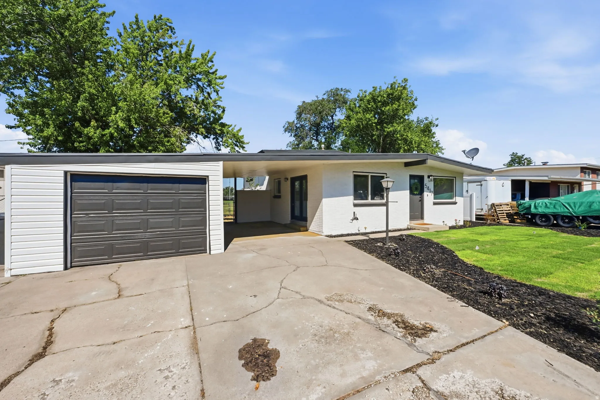 Single-story residence featuring a white stucco exterior, attached garage with a dark panel door, covered entry, and a manicured lawn area