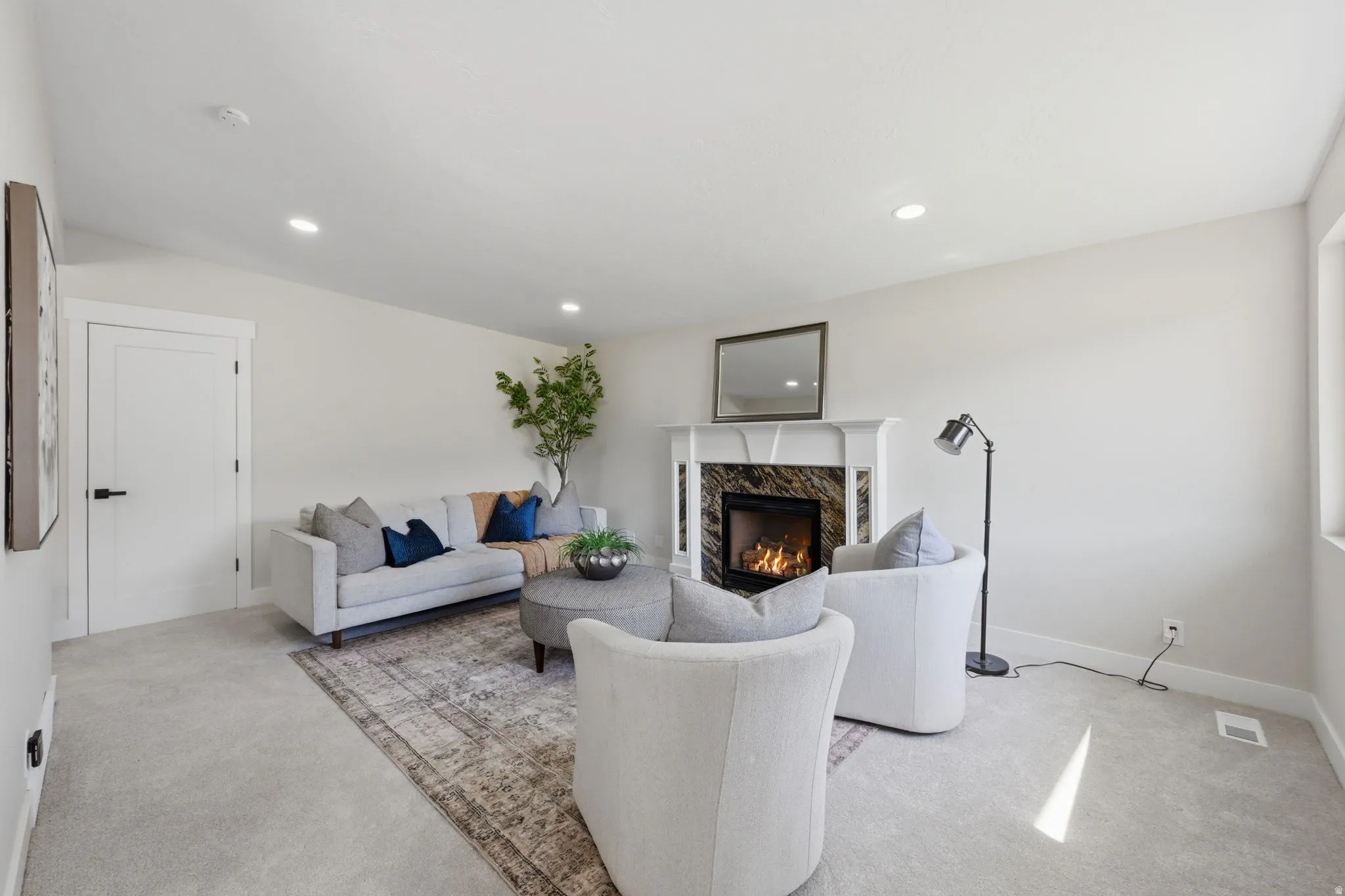Living area featuring a fireplace with a dark stone surround and white mantel, recessed lighting, light-toned carpeting, and a white door with dark hardware