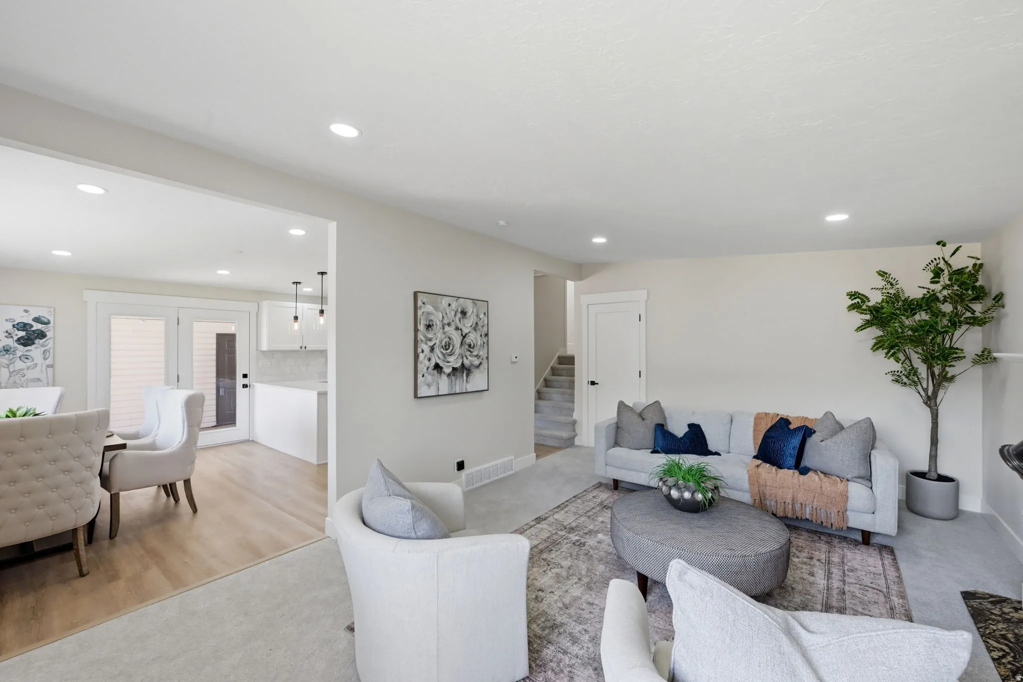 Bright open-concept living space featuring neutral wall tones, recessed lighting, and a blend of carpet and wood-finish flooring