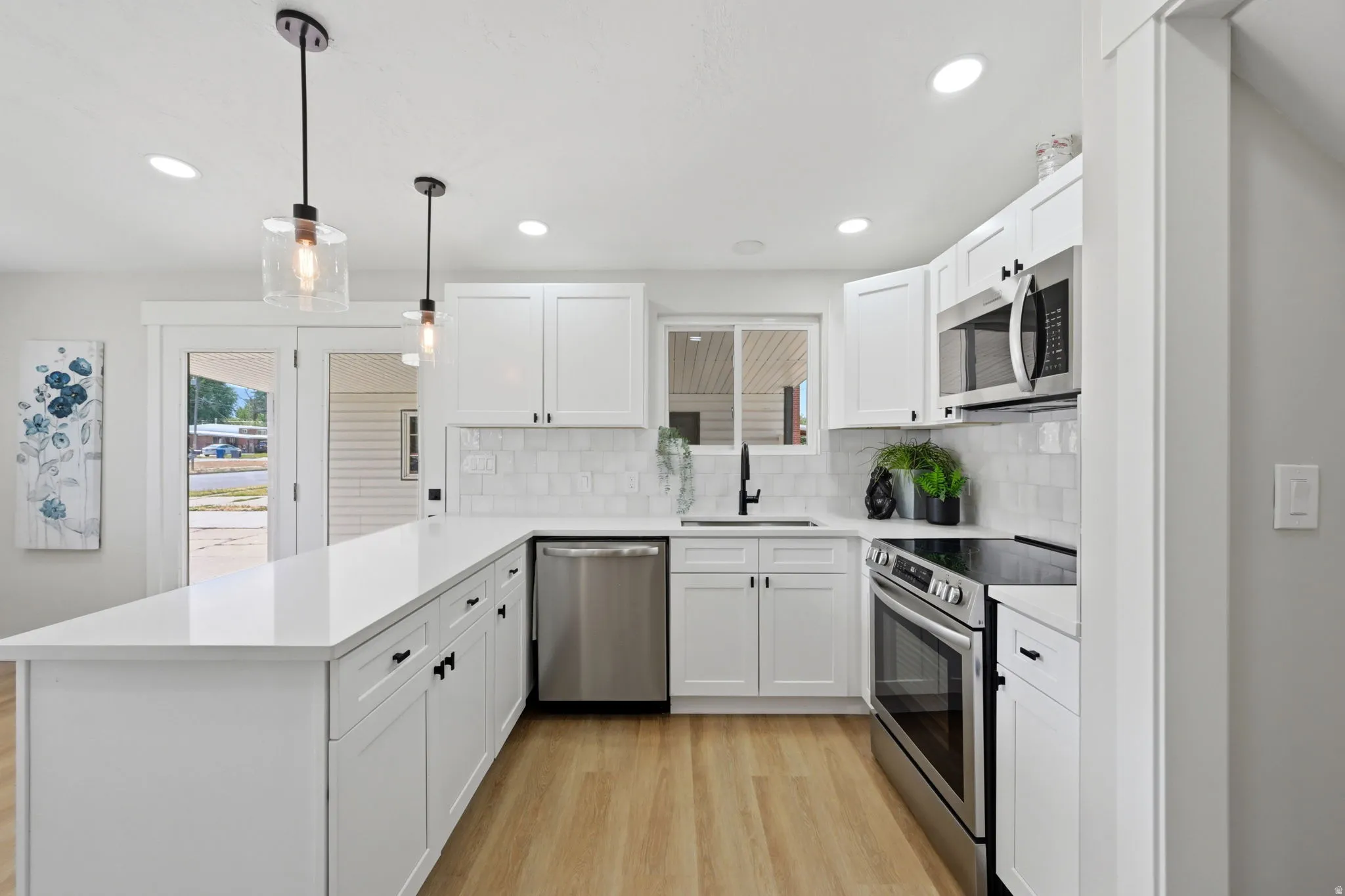 Modern kitchen featuring white shaker cabinetry, stainless steel appliances, light wood-finish flooring, and a spacious island with a white countertop