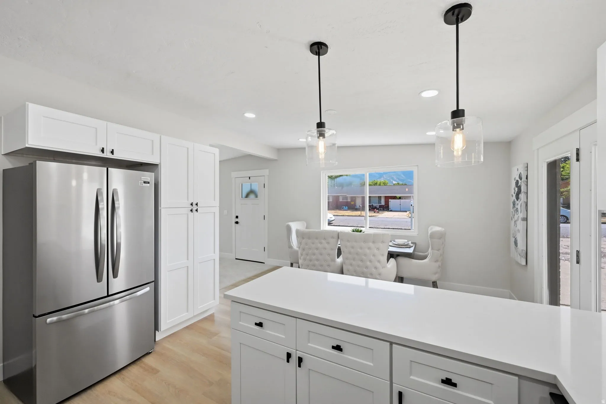 Bright kitchen featuring a stainless steel refrigerator, white cabinetry, a large kitchen island with white countertop, wood-finish flooring, and pendant lighting