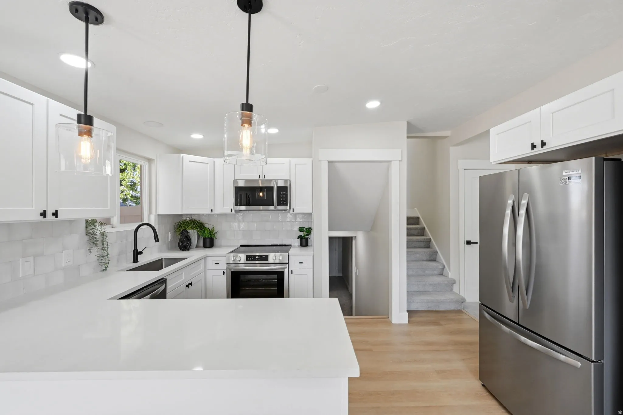 Modern kitchen featuring white cabinetry, stainless steel appliances, light-toned wood-finish flooring, and white countertops