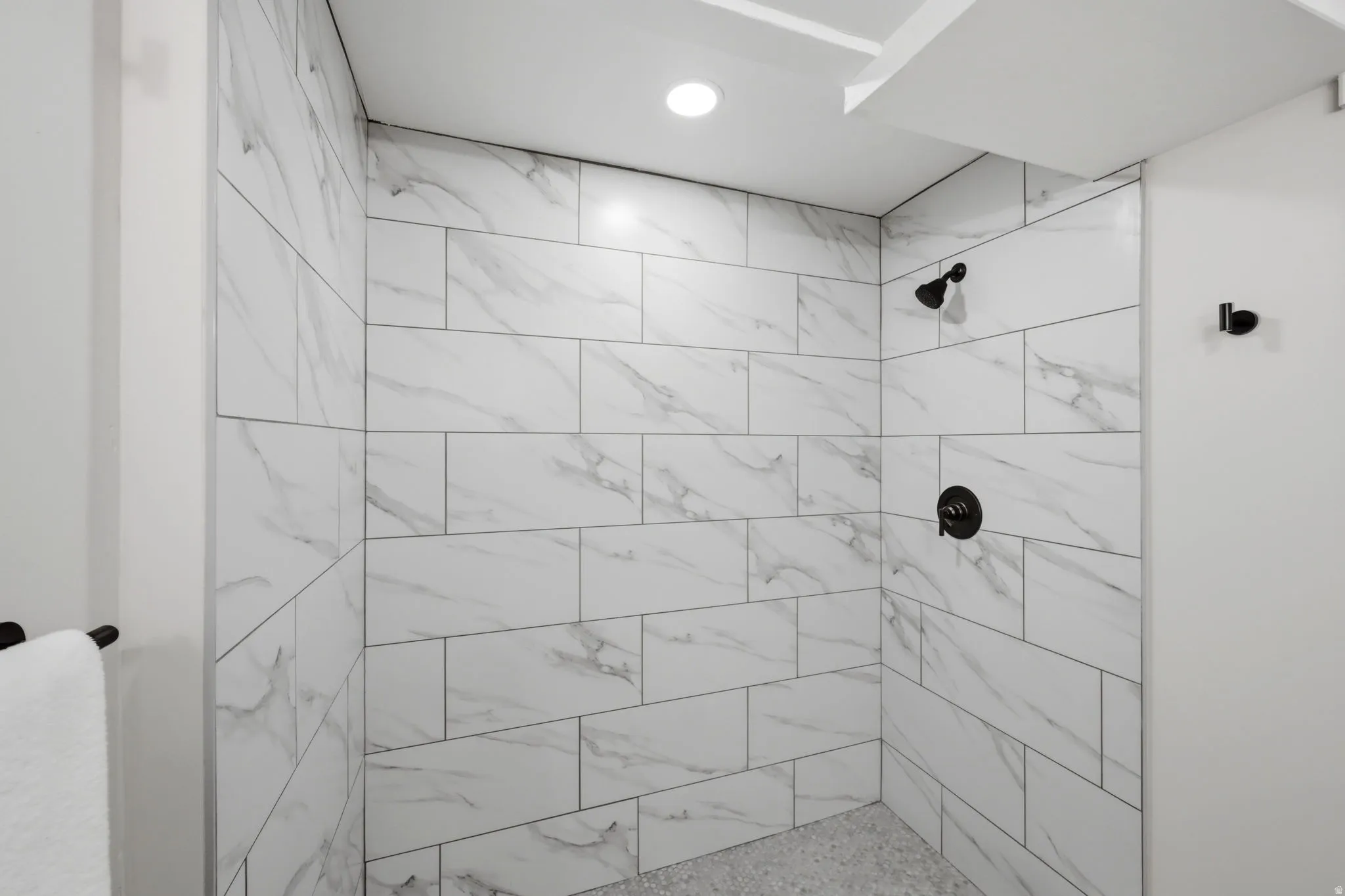 Shower enclosure featuring white marble-look subway tiles, black shower fixtures, a recessed ceiling light, and a complementary tiled floor