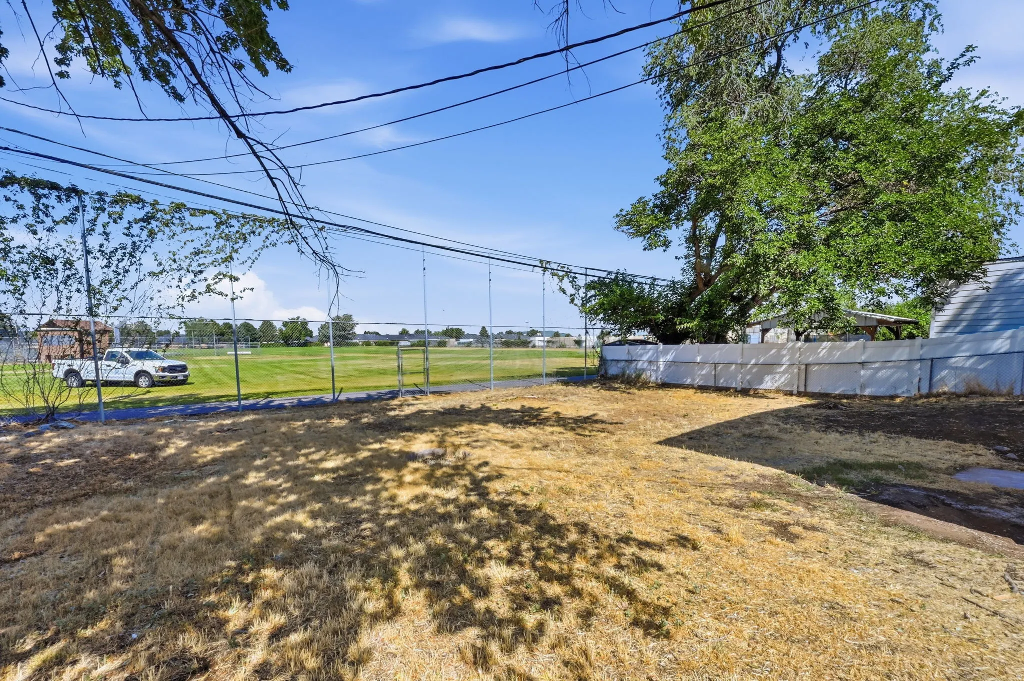 Expansive backyard with a chain-link fence bordering a large green field