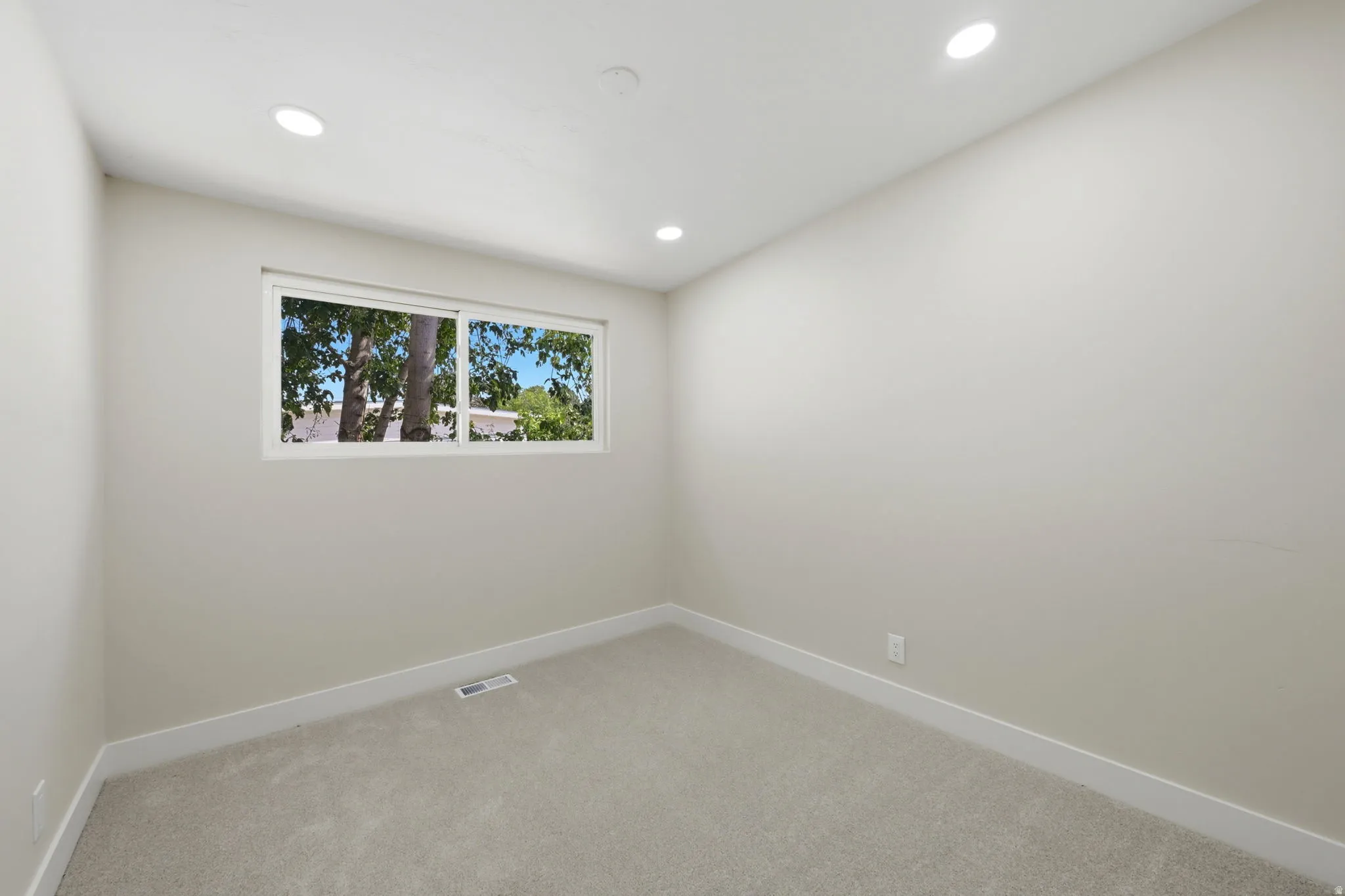 Room featuring a window with exterior tree scenery, recessed lighting, neutral-toned walls, plush carpeting, and white baseboards