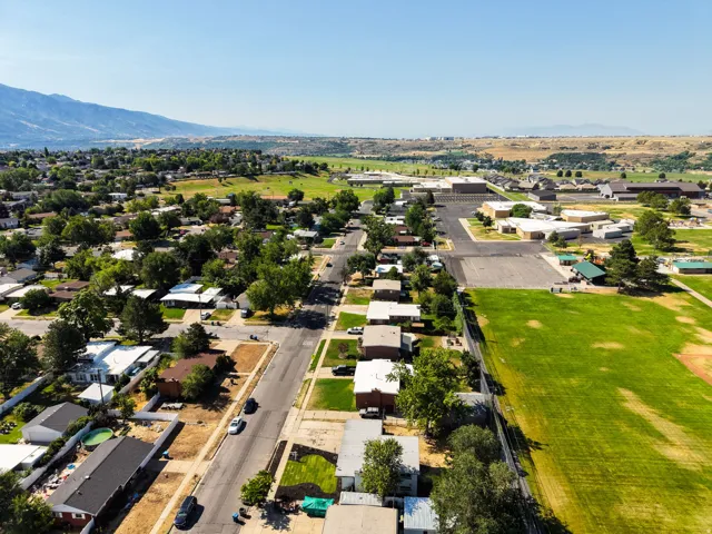 Aerial perspective showcasing a residential neighborhood with tree-lined streets, surrounded by green fields, and backed by distant mountains