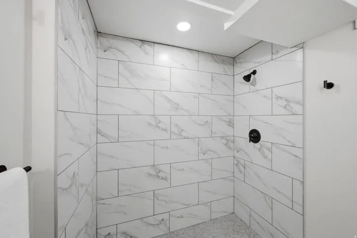 Shower enclosure featuring white marble-look subway tiles, black shower fixtures, a recessed ceiling light, and a complementary tiled floor