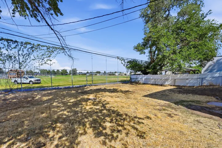 Expansive backyard with a chain-link fence bordering a large green field