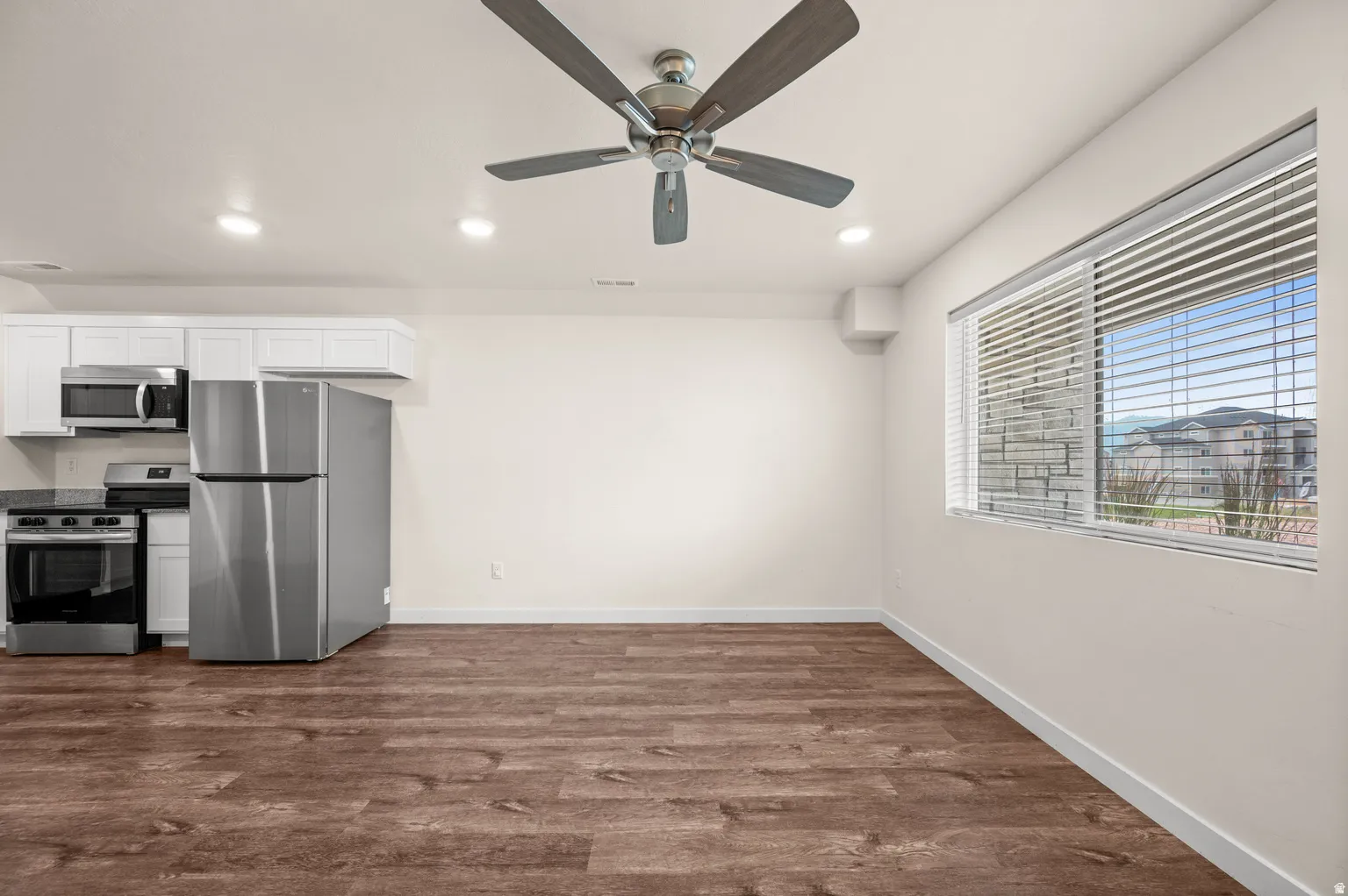 Open-concept living area with wood-finish flooring, white walls, and a modern ceiling fan