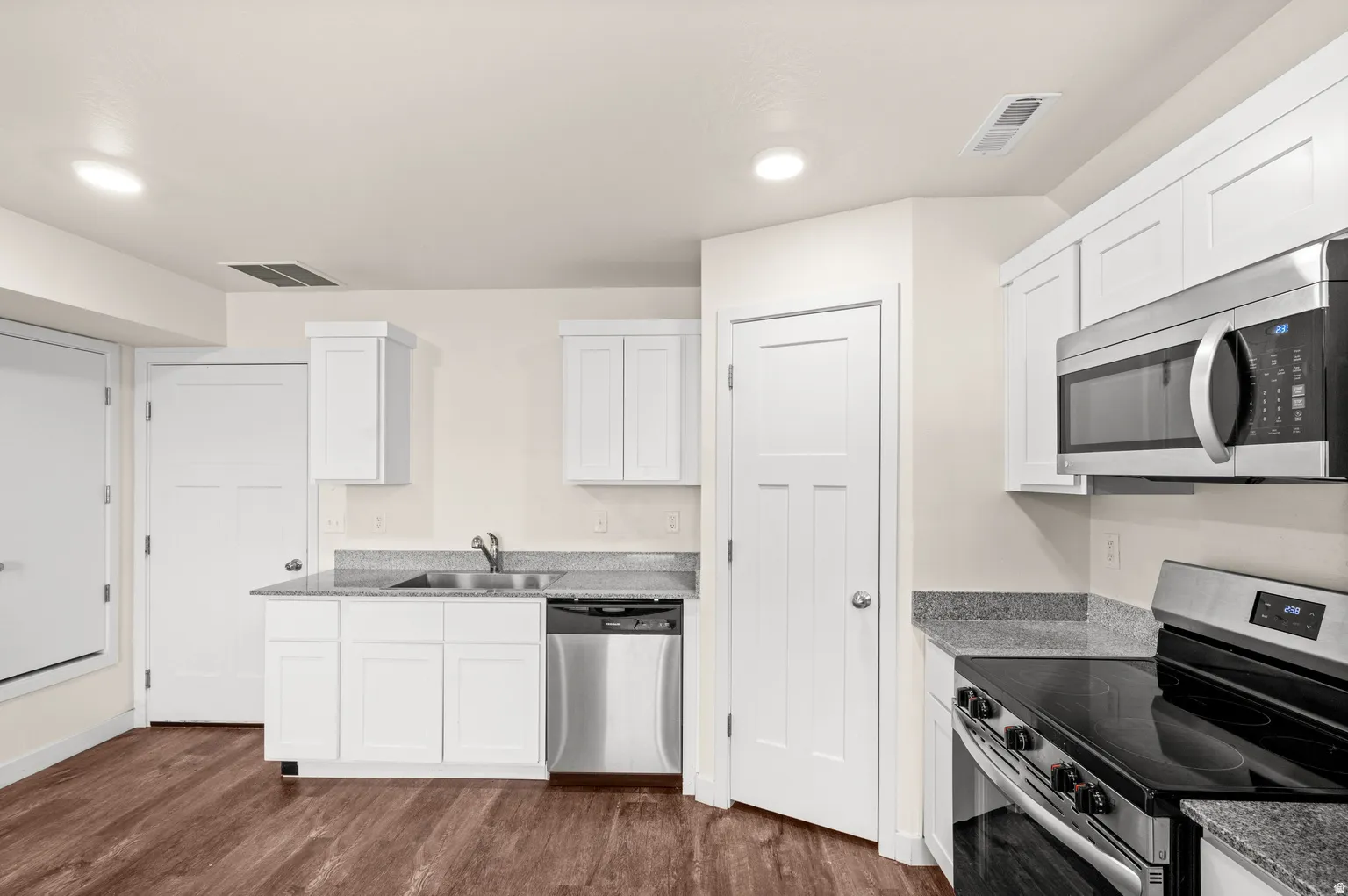 Kitchen featuring white cabinetry, grey speckled countertops, stainless steel appliances, wood-finish flooring, and recessed lighting