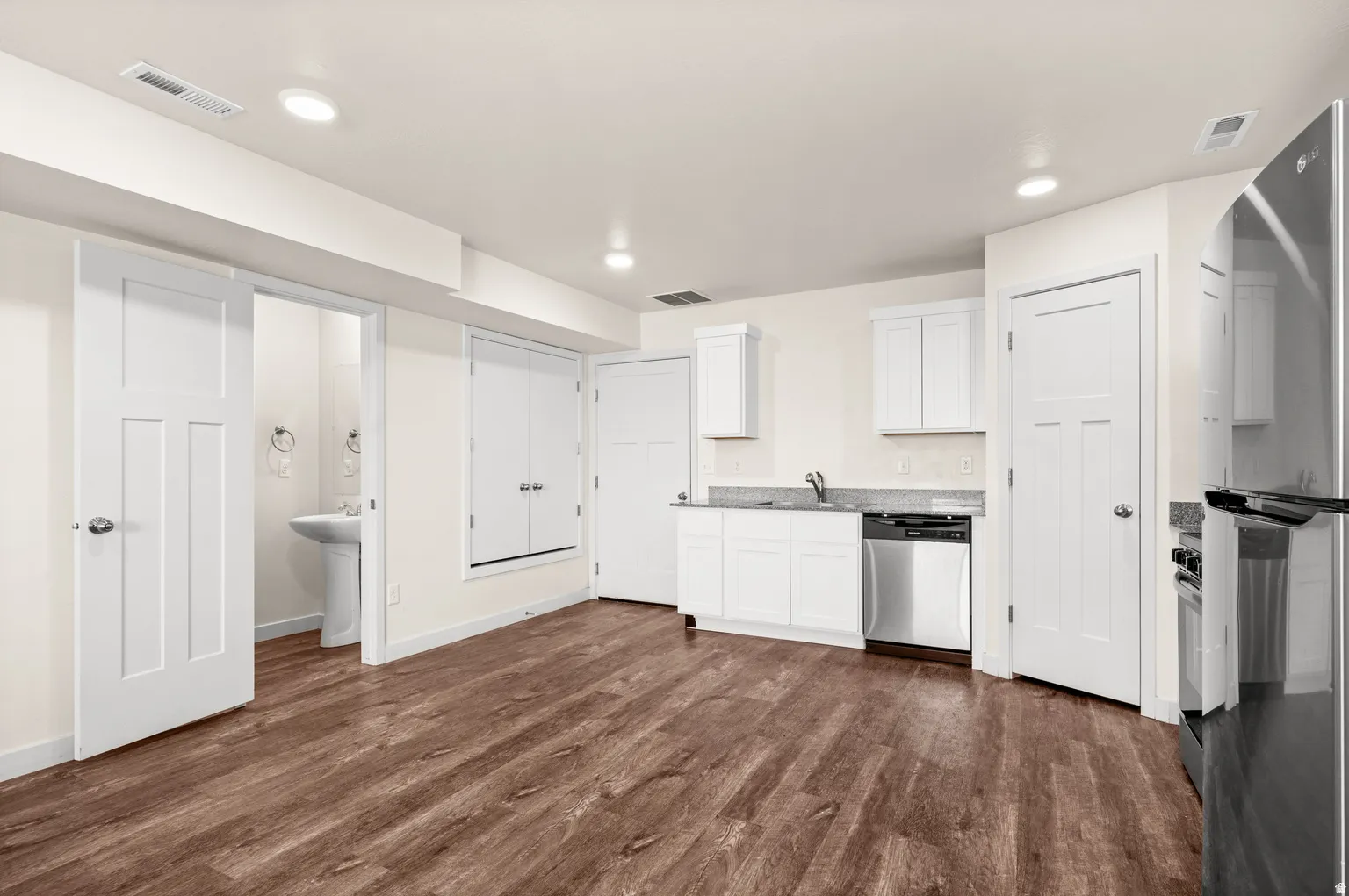 Open-concept room featuring wood-finish flooring, recessed lighting, and a kitchen area with white cabinetry, a stainless steel dishwasher, and a refrigerator