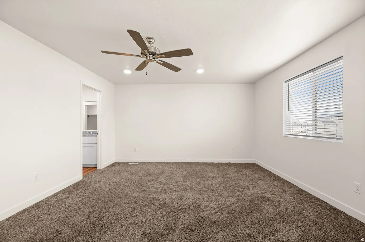 Spacious room featuring neutral carpeting, white walls, a window with horizontal blinds, recessed lighting, and a ceiling fan