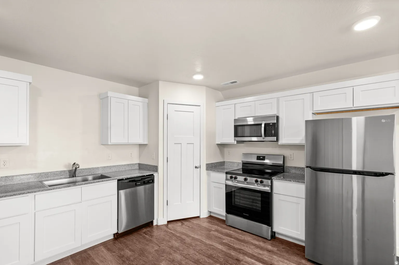 Kitchen featuring white shaker cabinetry, speckled countertops, stainless steel appliances, and wood-finish flooring