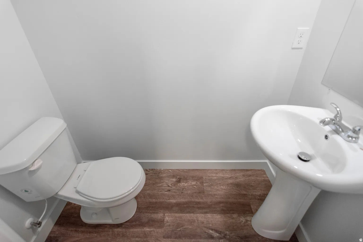 Powder room featuring a white pedestal sink with chrome faucet, a white toilet, and wood-finish flooring