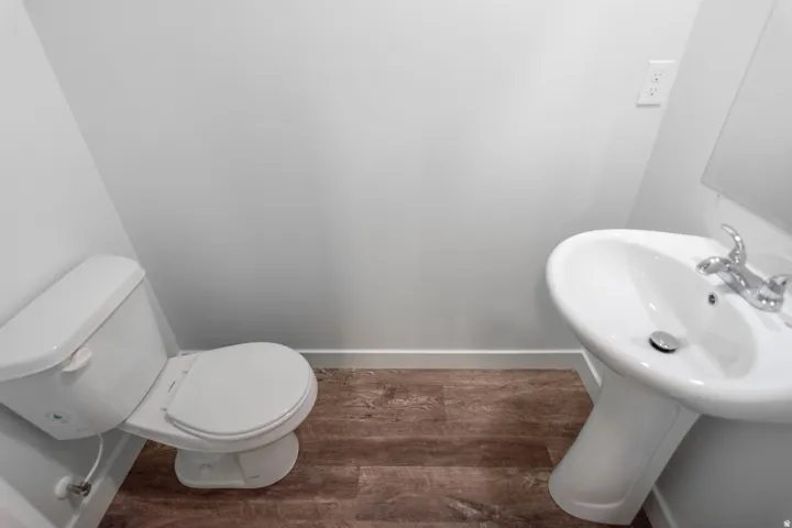 Powder room featuring a white pedestal sink with chrome faucet, a white toilet, and wood-finish flooring