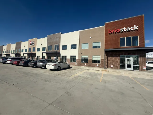 Commercial building exterior featuring a multi-toned facade, expansive parking lot, brick accents, multiple large windows, and a prominent entry