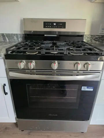 Stainless steel range with a five-burner gas cooktop, digital control panel, and a visible oven interior