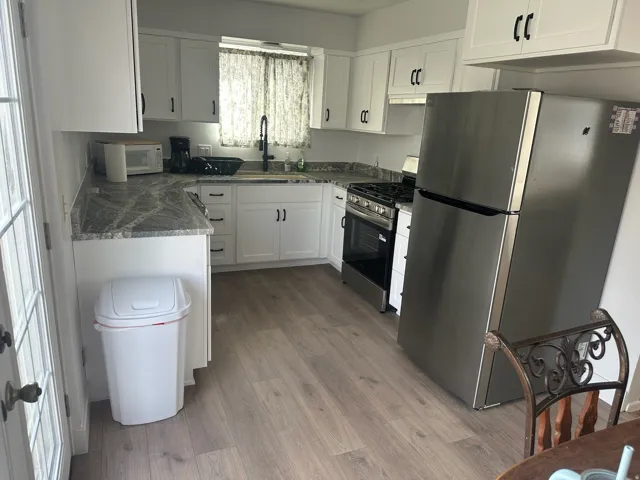 Kitchen with light wood-finish flooring, white cabinetry with black hardware, and dark patterned countertops