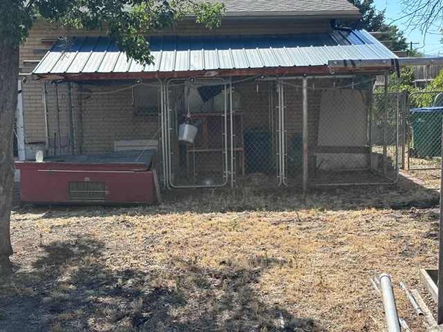 Chain-link enclosure with a sloped metal roof, situated against a brick exterior, featuring a red base unit