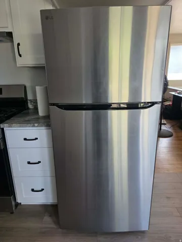 Stainless steel refrigerator with a bottom freezer, white cabinetry, dark stone-finish countertops, and wood-finish flooring