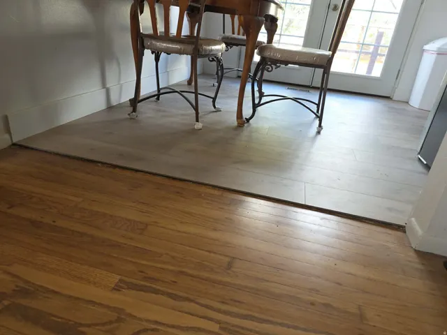 Rich wood-finish flooring transitioning to light wood-finish flooring, featuring a white baseboard trim and a glass-paneled door
