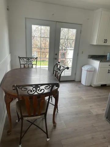 Dual glass-paned doors opening to an exterior space, featuring modern wood-finish flooring and white cabinetry with dark hardware