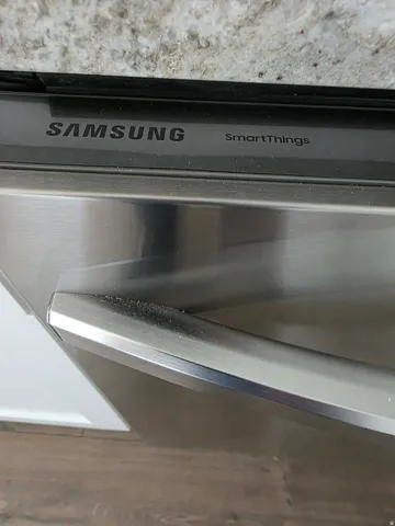 Stainless steel dishwasher with a granite-style countertop, white cabinetry, and wood-finish flooring