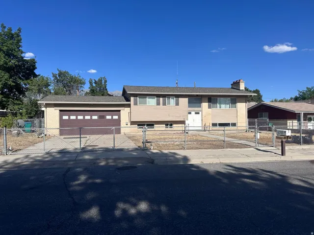 Split-level residence featuring a two-car garage with a brown door, light beige siding, and a fenced front yard