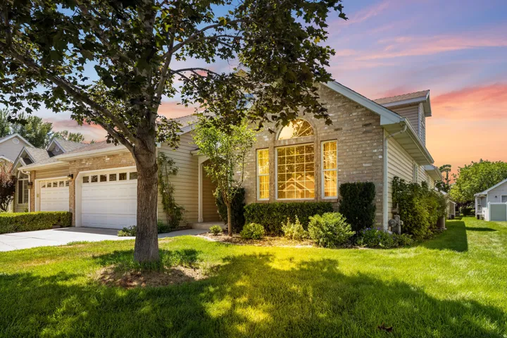 Brick and siding exterior featuring an arched window, a two-car garage, manicured shrubs, and a verdant lawn