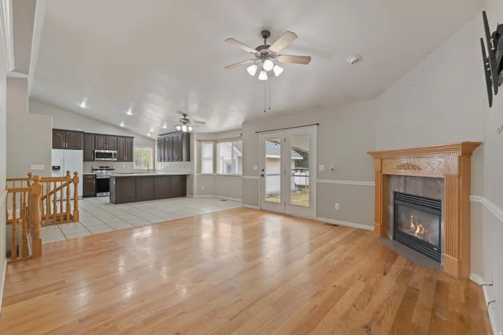 Open-concept living space featuring hardwood flooring, a fireplace with a light wood mantel, and vaulted ceilings
