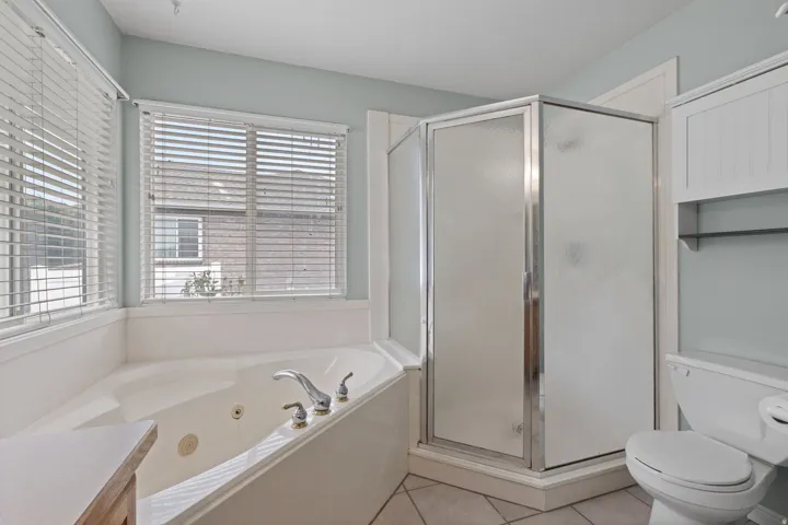 Bathroom featuring a corner jetted soaking tub with chrome fixtures, a glass-enclosed shower, and a toilet