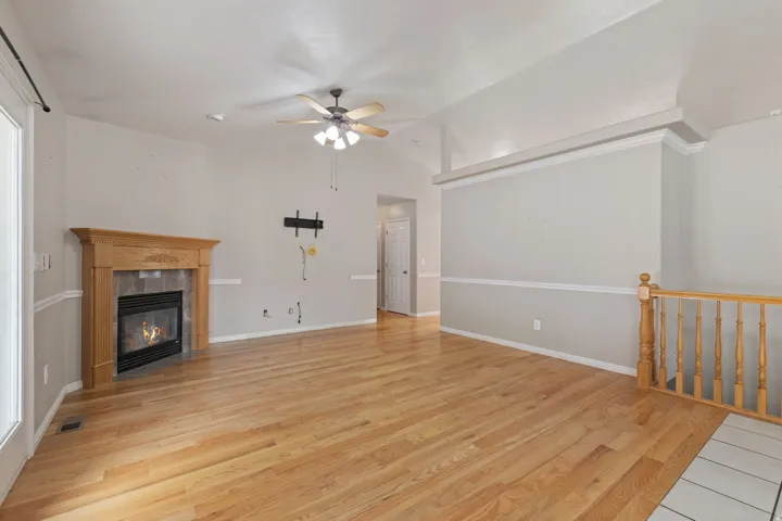 Spacious room featuring wood-finish flooring, a fireplace with a wood mantle and tile surround, and a ceiling fan with light fixture