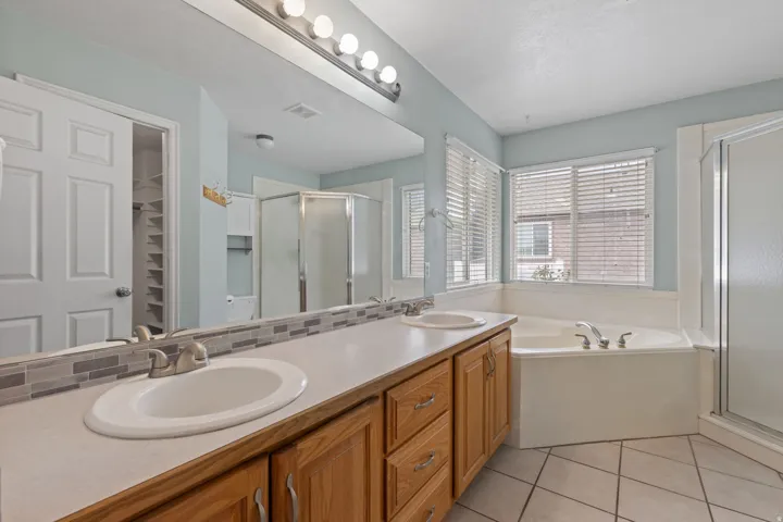 Bathroom featuring a double vanity with wood cabinetry, a large mirror, and a mosaic tile backsplash
