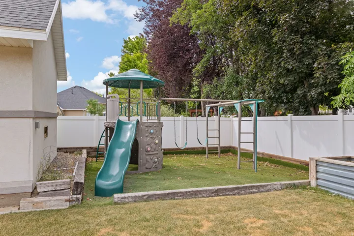 Fenced backyard featuring a playset with slide and swings, a metal raised garden bed, and wood-finish retaining timbers