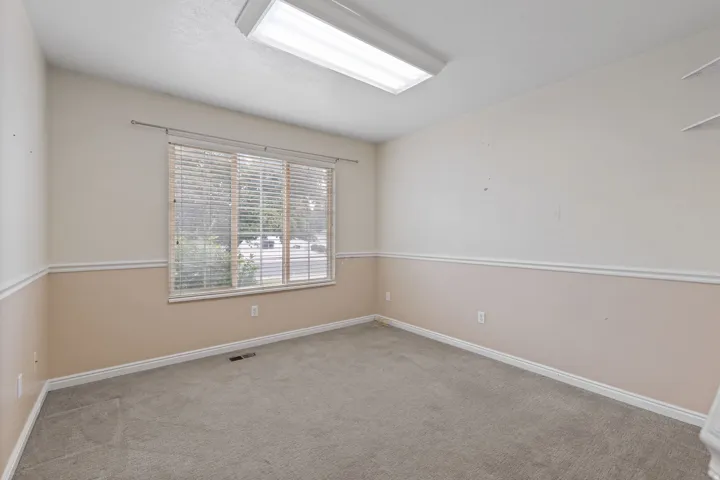 Neutral-toned room featuring a large window with blinds, light gray carpeting, and a two-tone wall treatment with chair rail molding