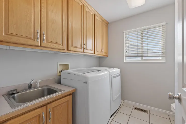 Dedicated laundry area featuring abundant cabinetry, a utility sink, and tile flooring