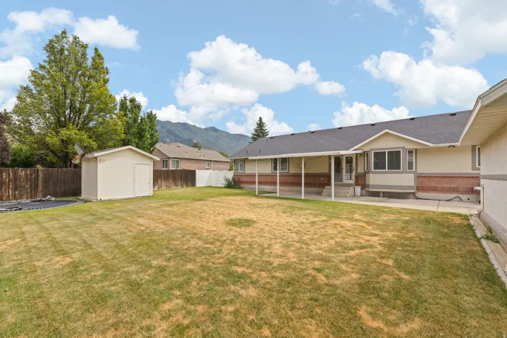Spacious backyard with a covered patio, featuring a storage shed and perimeter fencing