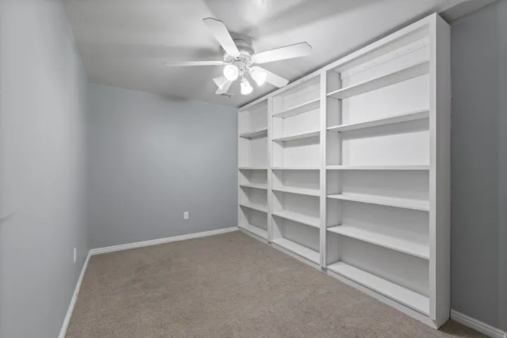 Room featuring a wall of built-in shelving, carpet flooring, and a ceiling fan with light fixture